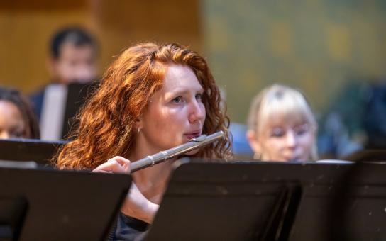 Flautist behind a music stand performing while watching the conductor