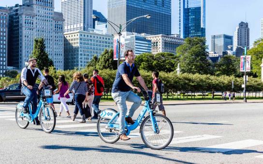 people walking and riding bikes near Chicago's lakefront, with buildings in the background