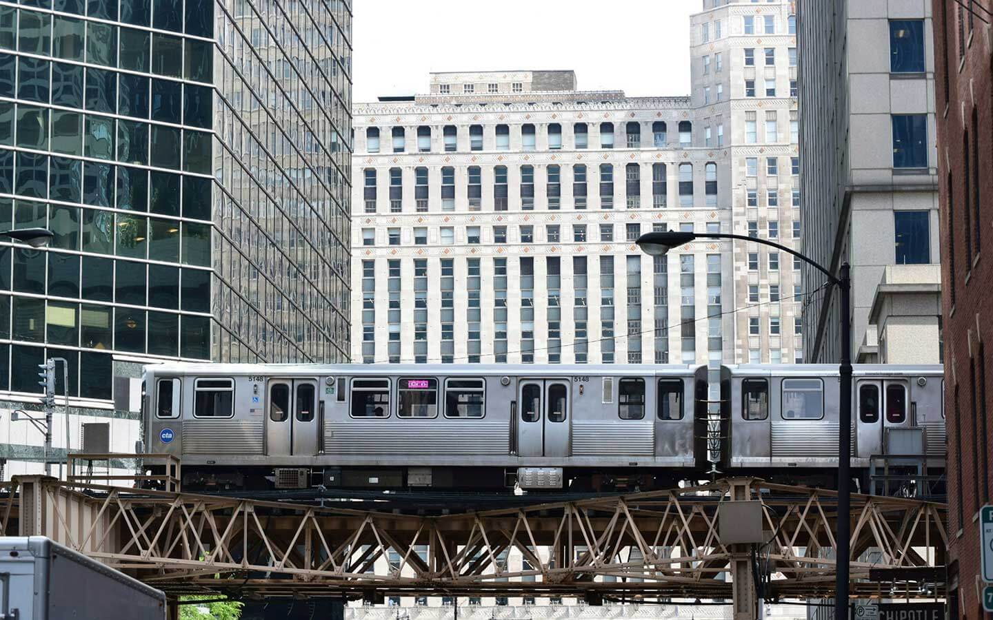 A landscape portrait of the Chicago Loop with elevated el train tracks with a train passing by in the foreground