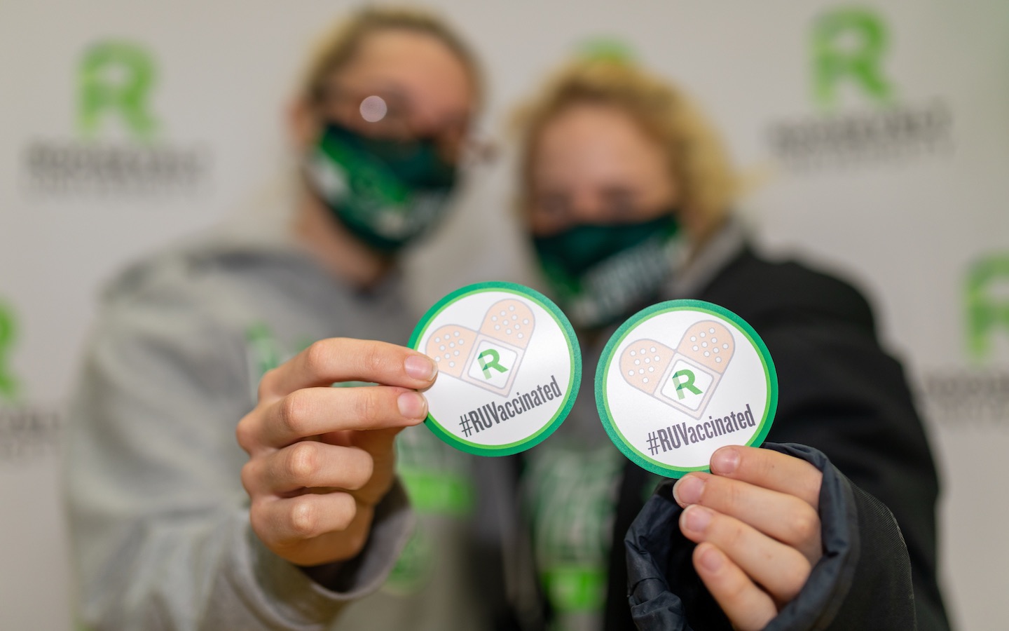 Two women in masks hold RUVaccinated stickers