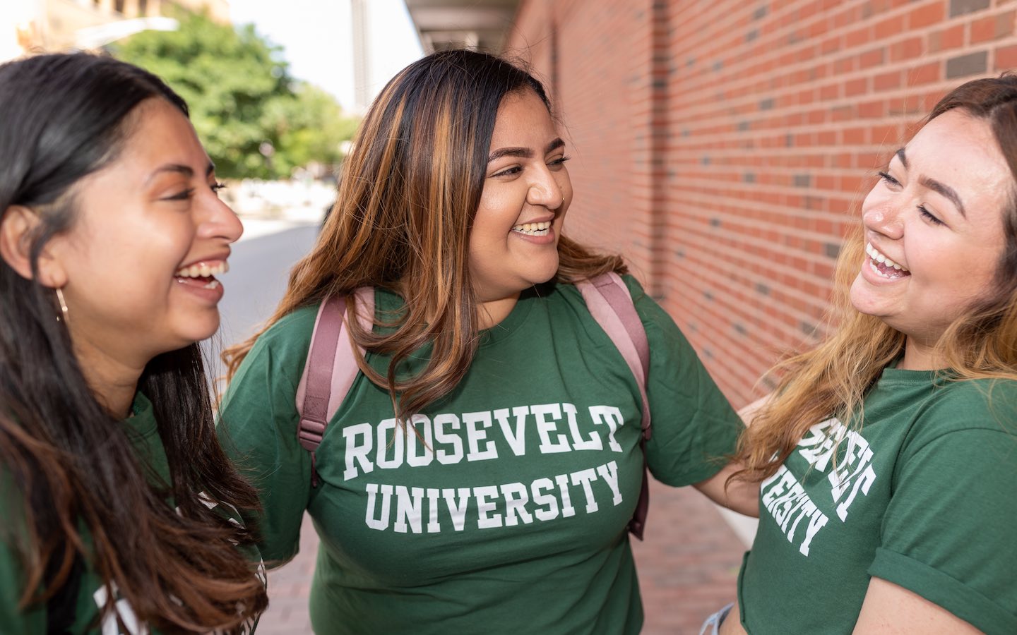Three Latina students in Roosevelt t-shirts smile at each other.