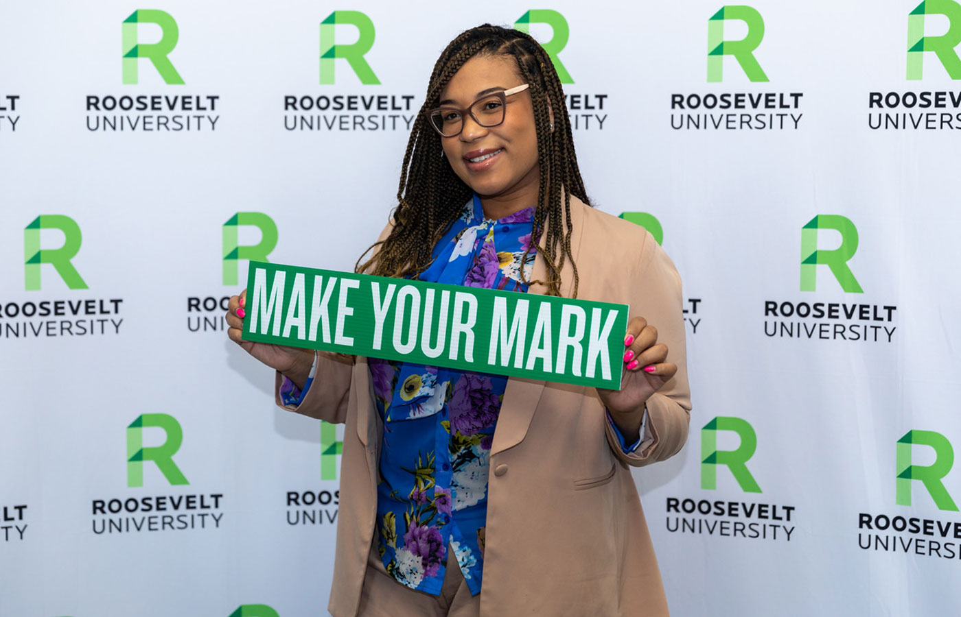 student holding "make your mark" sign in front of a Roosevelt University screen