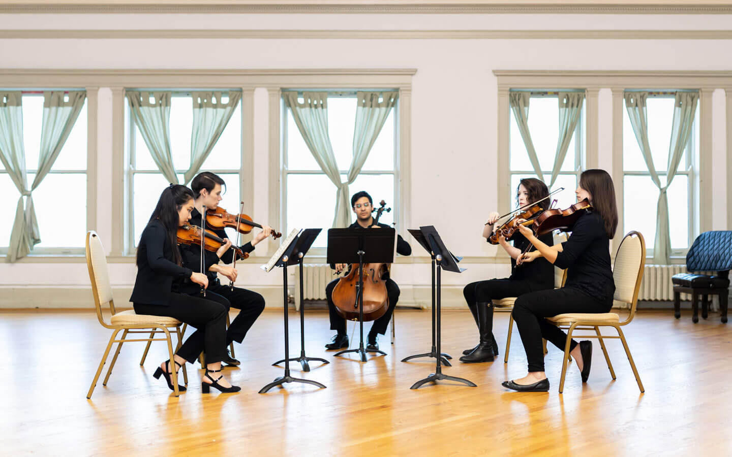 String quintet performing at a recital in a well-lit room full of natural lighting