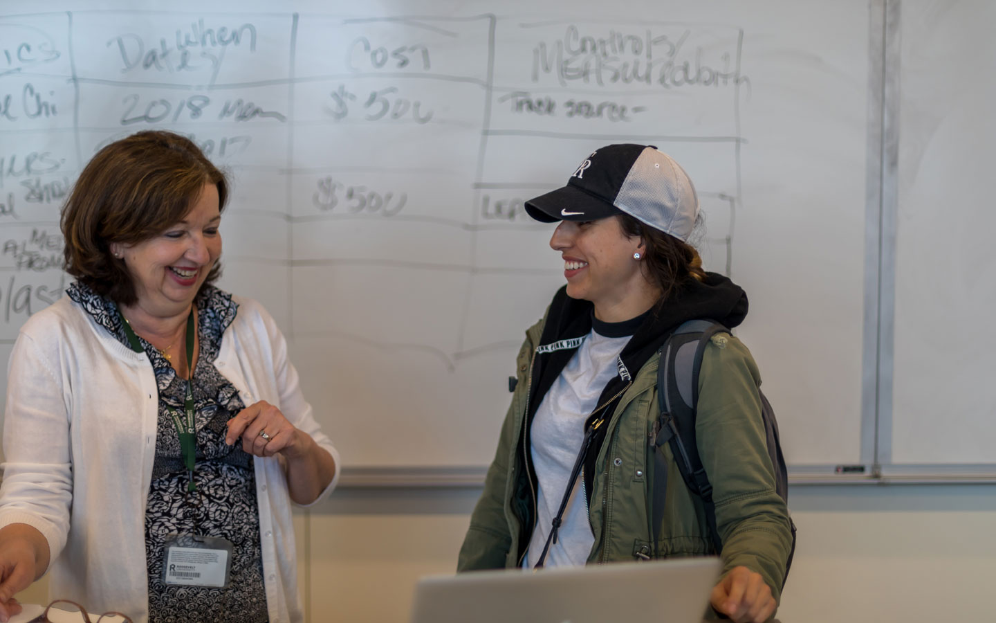 Student and instructor smiling in front of a classroom whiteboard.