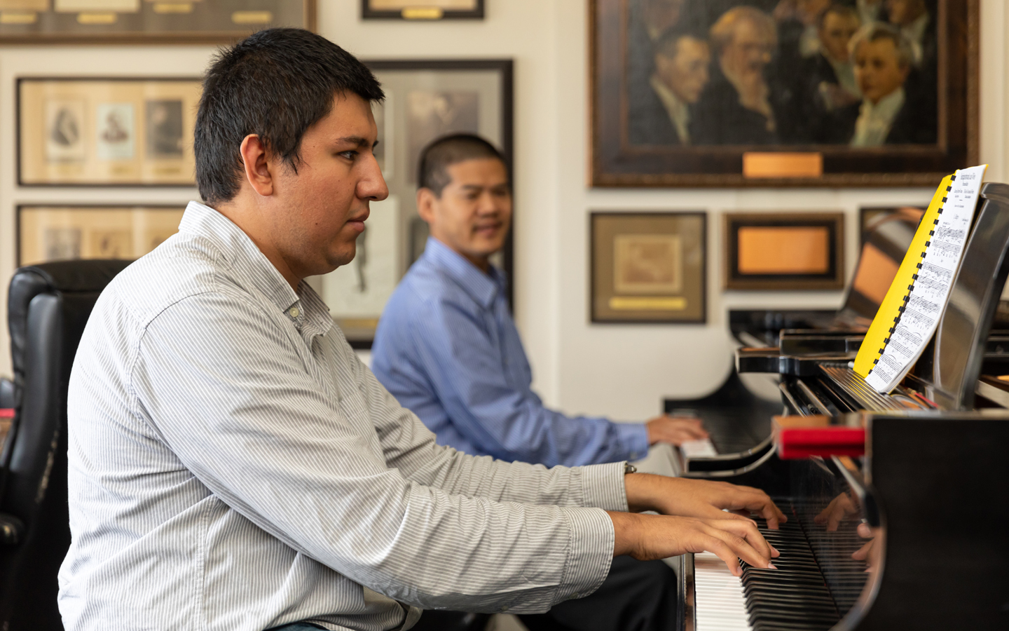 A student is playing the piano for a faculty member