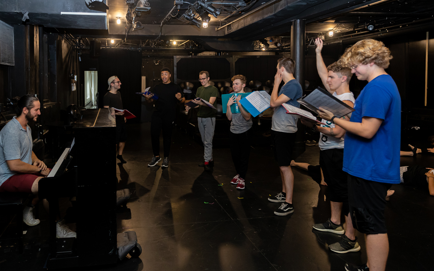 A small group of students standing around a piano practicing a voice performance