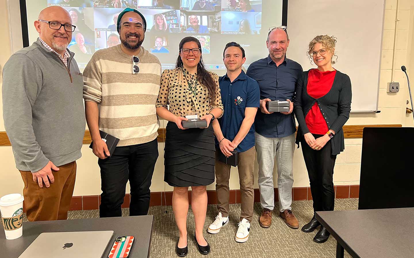 A small group of 2026 award winners stands in front of a screen.