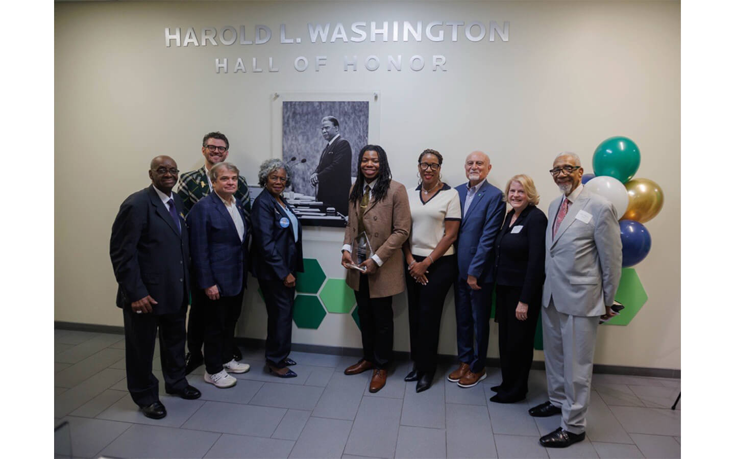 Honored guests, speakers, alumni, staff, and RU President stand in front of the Harold L. Washington Hall of Honor picture and dedication plaque.  