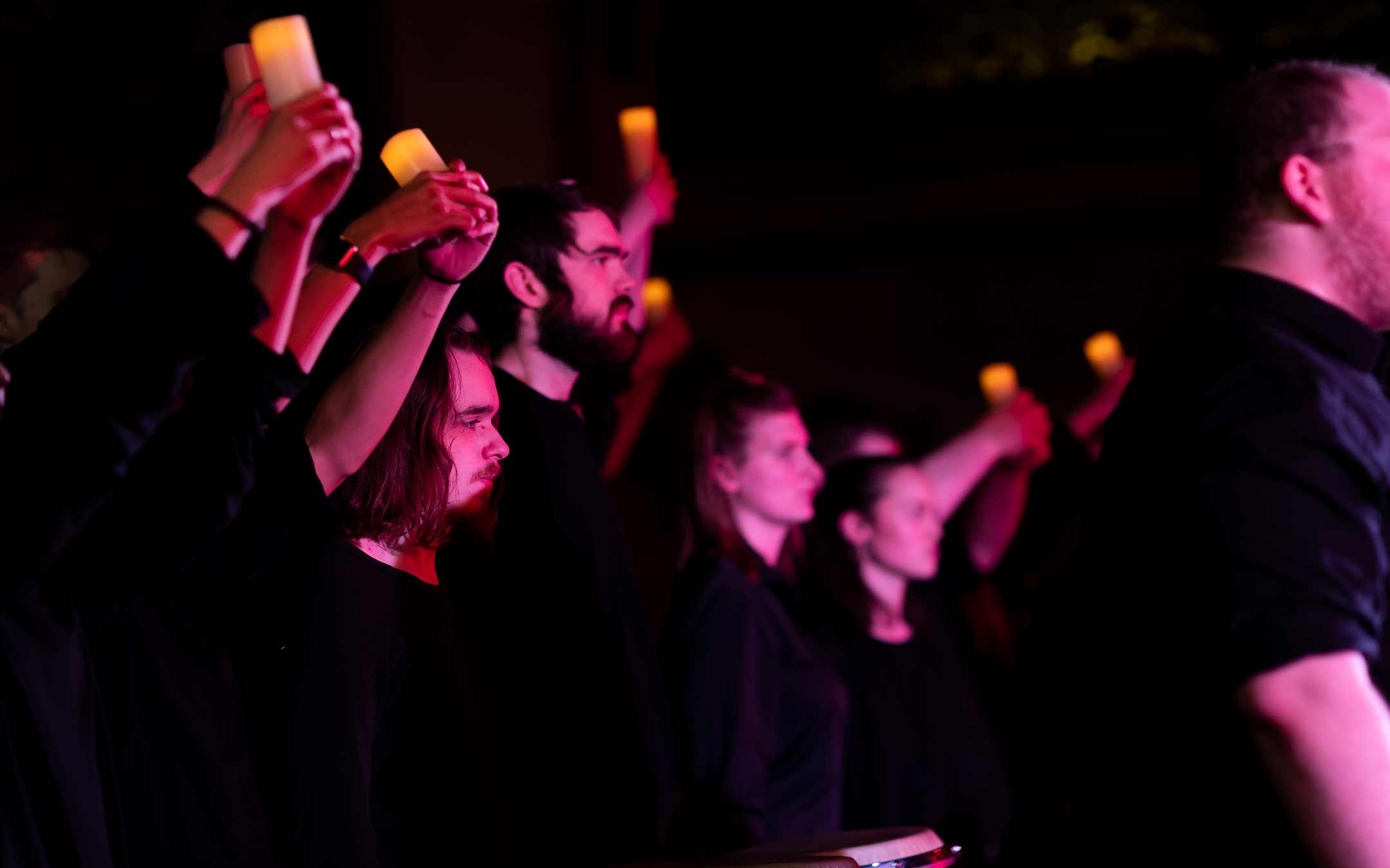 Students in a performance holding candles against a dark background