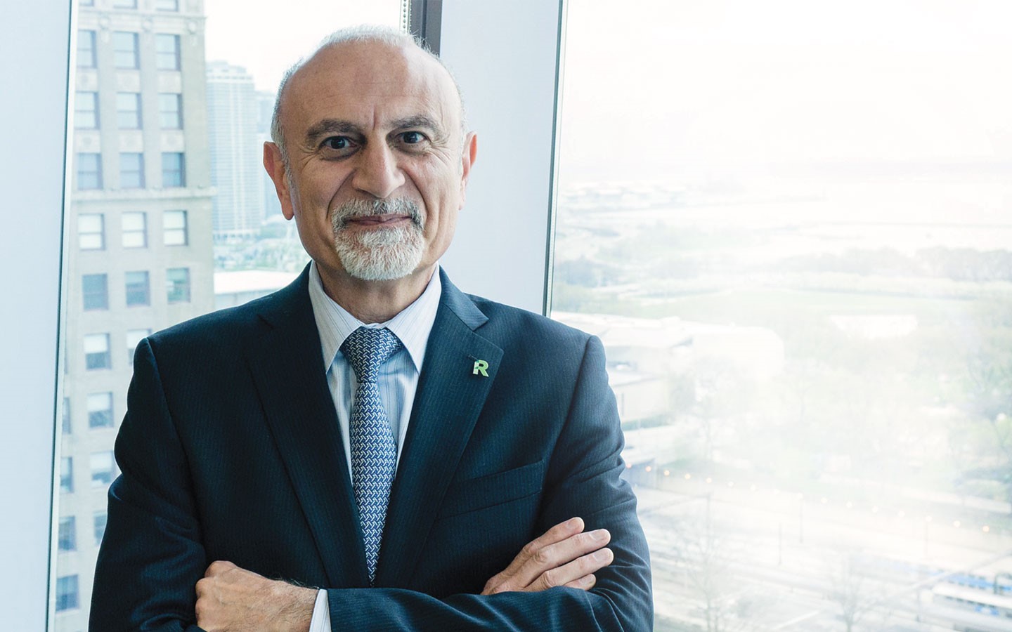 President Ali Malekzadeh stands in a suit with his arms crossed in front of windows