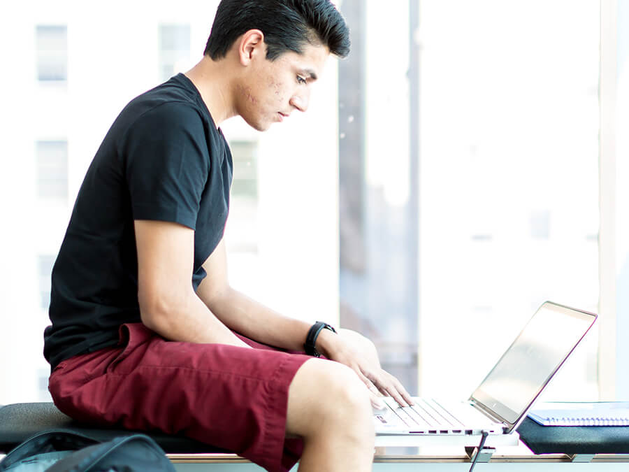 Student in red shorts at laptop - Summer Courses Online