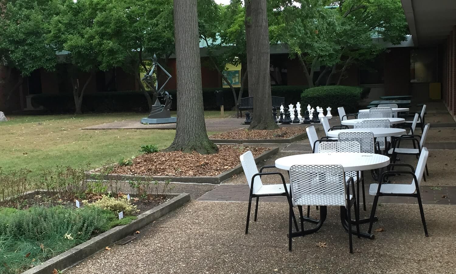Outdoor courtyard with trees, plants, benches and tables with chairs. 