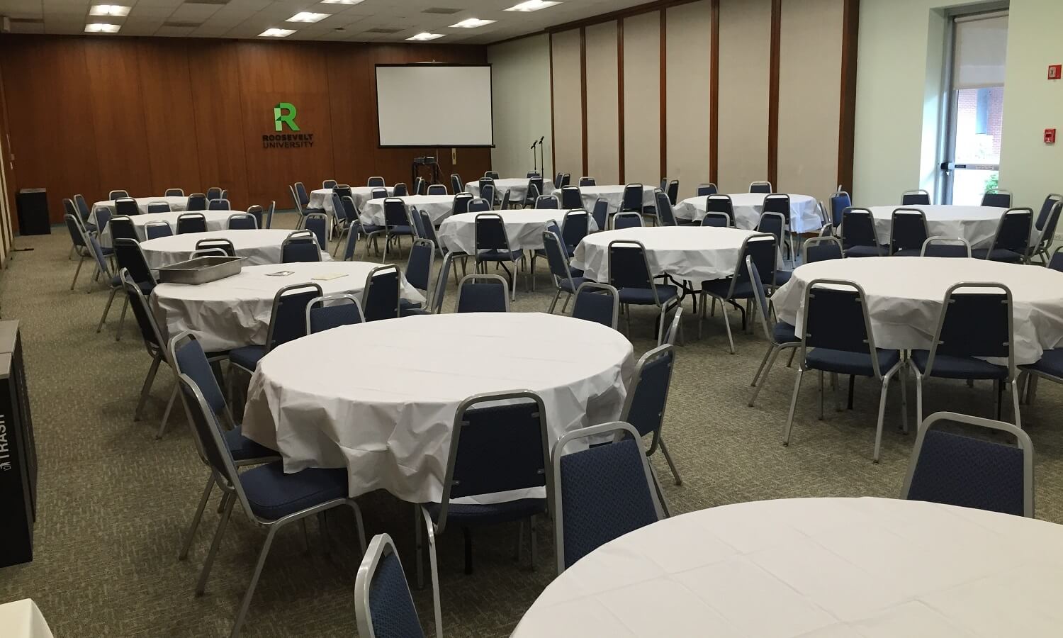 Large room with wood panelled walls featuring numerous round tables and chairs.