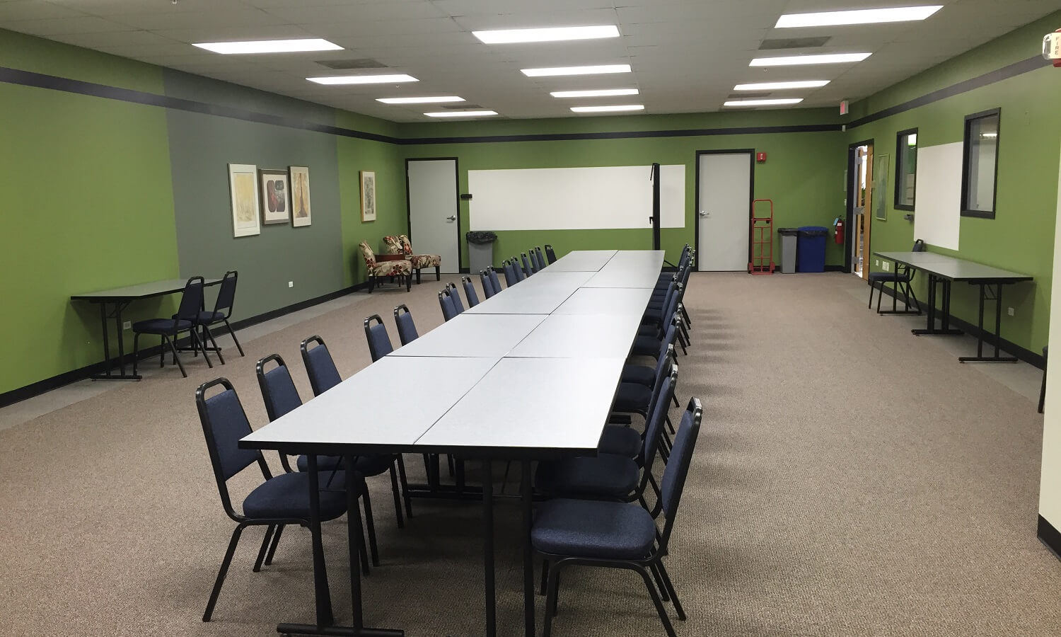 A mid-sized carpeted room with white boards and large alignment of tables and chairs.