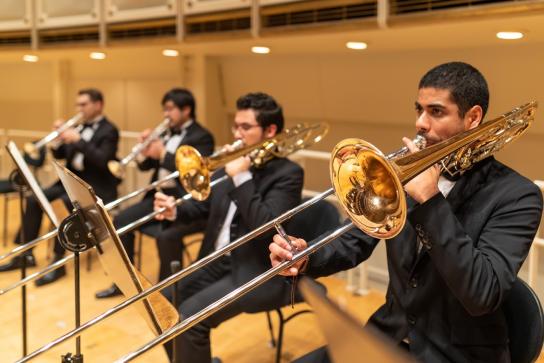 Musicians dressed in tuxedos playing the trombone.