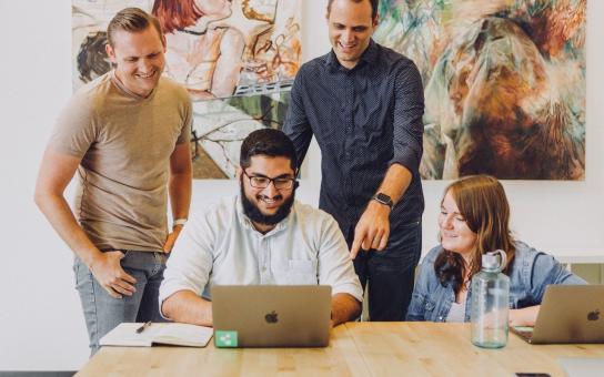 A group gathers around a computer to discuss a project 