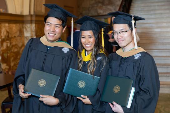 A small group of students in graduation cap and gown posing with diplomas