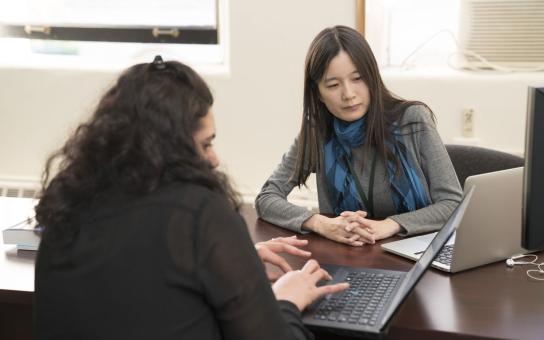 Two people meeting across and office desk, each sharing their view of their laptop screen with each other.