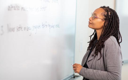 Instructor facing a whiteboard with unknown subject material displayed on the board.