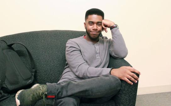 Student sitting on a lounge sofa with one arm leaning on the arm rest and their backpack next to them