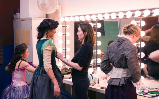 Three theatre students in costumes are making their final adjustments to their wardrobe