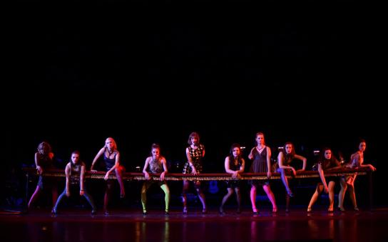 A dark stage setting with 10 performers each having a different color wardrobe