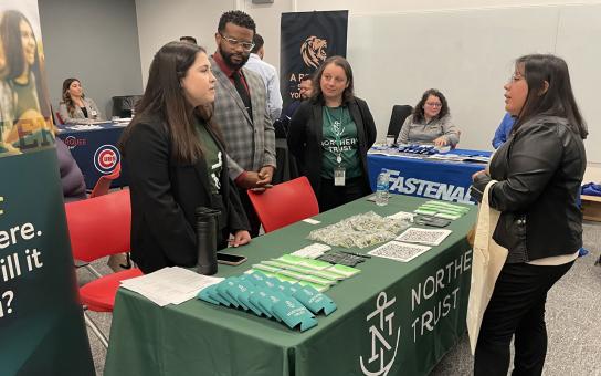 A student standing in in front of table at career fair talking with employers