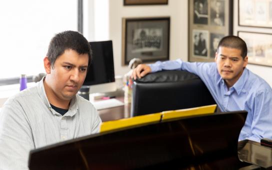 Student sitting at a piano while the instructor sits near by watching the student practice