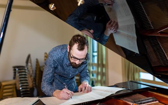 A student standing in by a computer bent over to write on sheet music