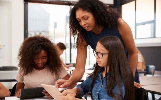 Instructor Assisting young students with reading on a tablet