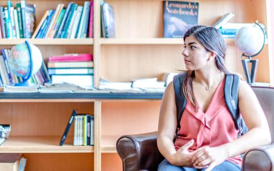 Female student sitting on a single-seat sofa in front of bookshelves