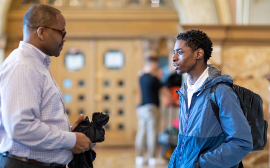 Student in jacket and backpack having a conversation with the a faculty member in the Auditorium building lobby.