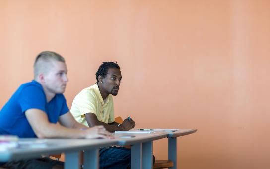 Student sitting behind a table in the classroom setting, leaning forward and looking attentive