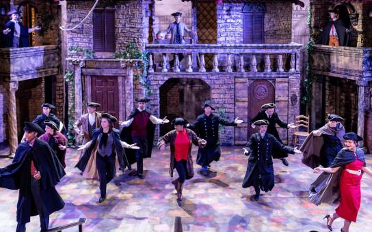 Performers in Victorian era costume dancing in front of Victorian era background.