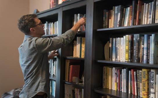 Man selecting a book from a large bookshelf full of books.