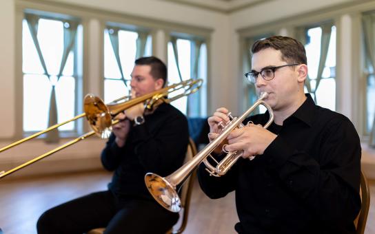 Two students in black shirts playing brass instruments; one a trombone and the other a trumpet