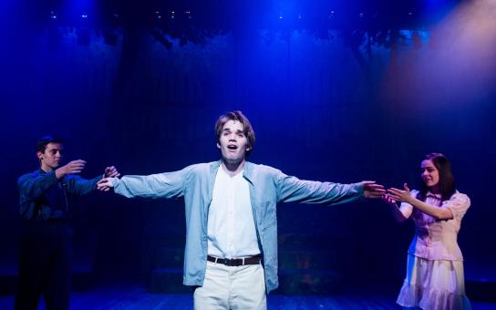 Student standing center stage with arms outstretched singing in a musical performance