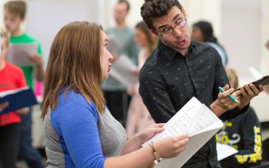 Two students holding music books, while looking at each other while harmonizing their voices