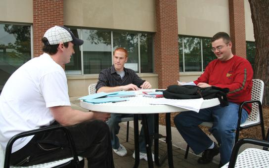 Three students seated at a table in the Schaumburg campus courtyard
