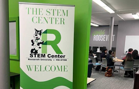 Welcome sign at the entrance of the STEM Center; students are seen working at a table in the background
