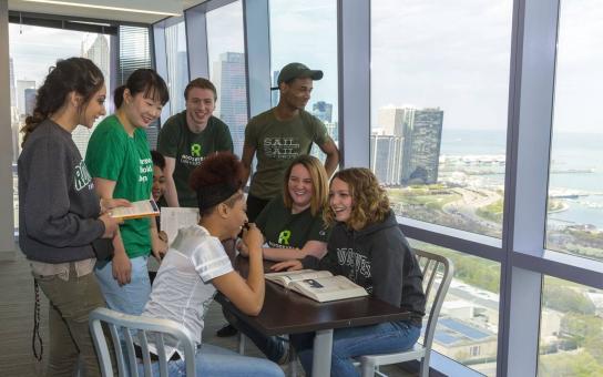 Students gathered a around a table in front of windows overlooking Lake Michigan