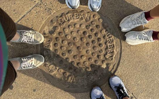 Four sets of shoes stand adjacent to a manhole cover marked Durban, South Africa