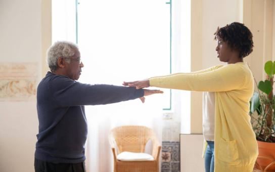 Two adult facing each other with arms outstretched engaging in physical therapy