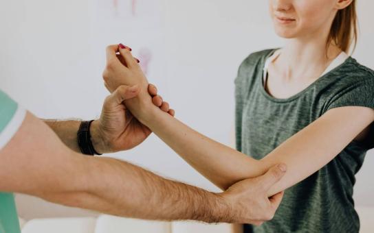 A person holding another person's arm by the wrist and elbow engaged in physical therapy