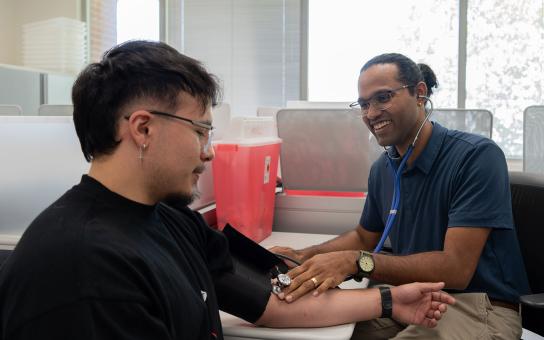 A smiling medical professional takes the blood pressure of someone with their arm outstretched on a table