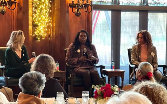 Panel of women sitting on platform in front of audience at a luncheon.