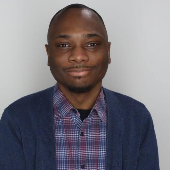 Student Charles Hill, PsyD ‘28 Doctorate in Clinical Psychology Candidate, wearing a multi-colored button down shirt with a gray sweater