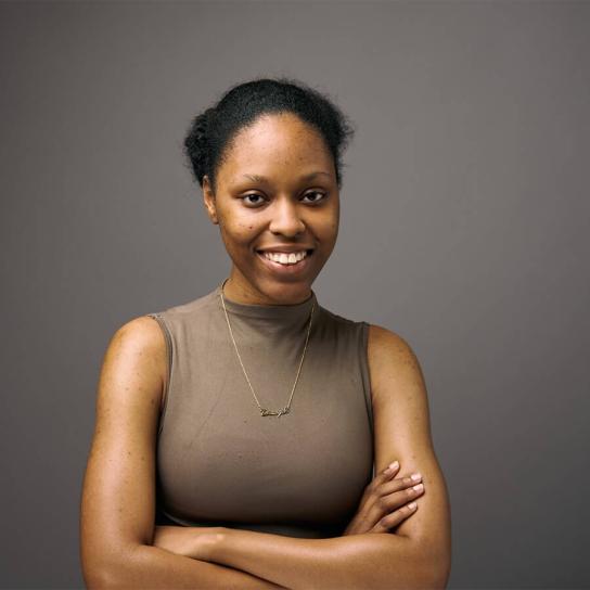Student Danijah Davis, BA ‘26 Organizational Leadership Student, smiling and posing with arms crossed wearing a brown sleeveless shirt