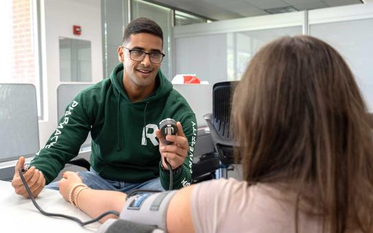 Student in a Pharmacy sweatshirt takes a patient's blood pressure