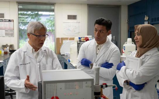 Students in lab coats listening to instructor in lab coat explaining medical equipment